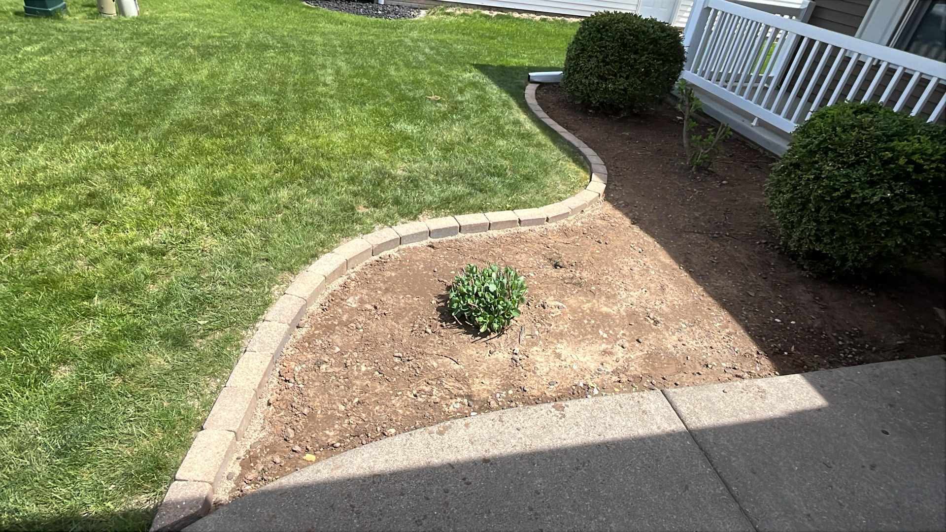 Paver-edged landscape bed cleared and prepped for planting next to a mowed lawn