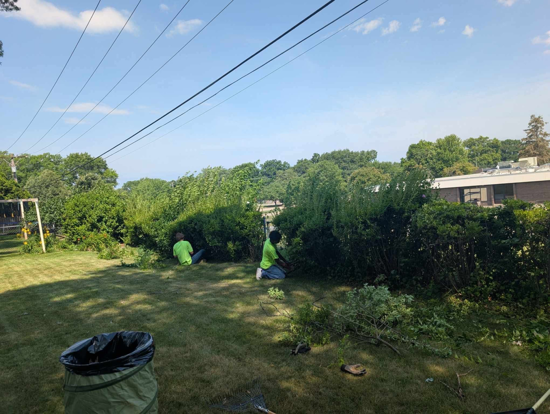 Two Yardsmith Solutions crew members hand-trimming an overgrown hedge line in a backyard