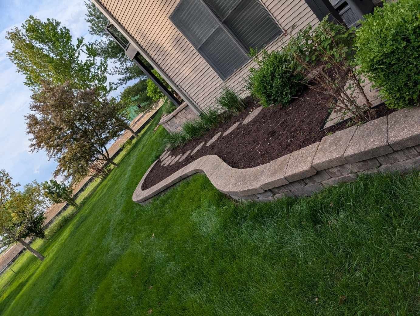 Curved block retaining wall bed refreshed with dark mulch and trimmed shrubs